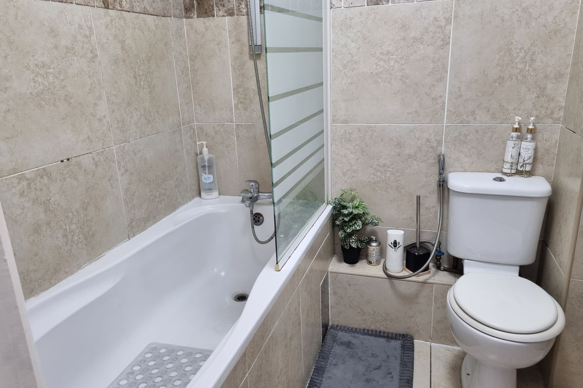 A functional bathroom featuring a bathtub with a glass shower screen, tiled wall finishes, and a standard toilet.