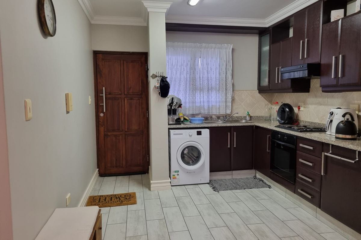 A functional kitchen featuring dark wood cabinetry, granite countertops, built-in oven and hob, and tiled flooring with an integrated laundry area.