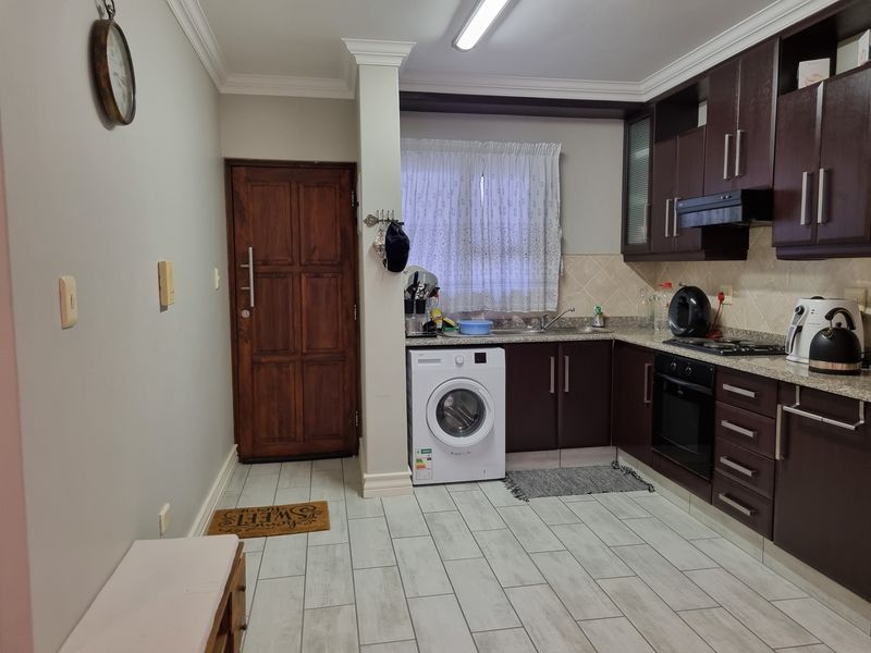 A functional kitchen featuring dark wood cabinetry, granite countertops, built-in oven and hob, and tiled flooring with an integrated laundry area.