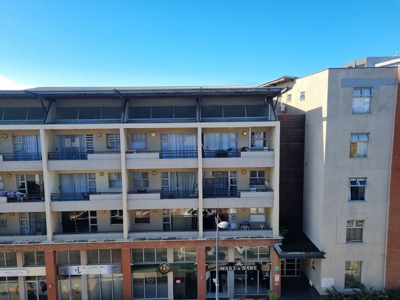 Exterior view of a multi-story apartment building featuring private balconies, sliding glass doors, and ground-floor commercial retail spaces.
