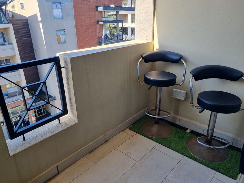 A compact apartment balcony featuring tiled flooring and a metal balustrade, offering an urban view of the surrounding residential buildings.