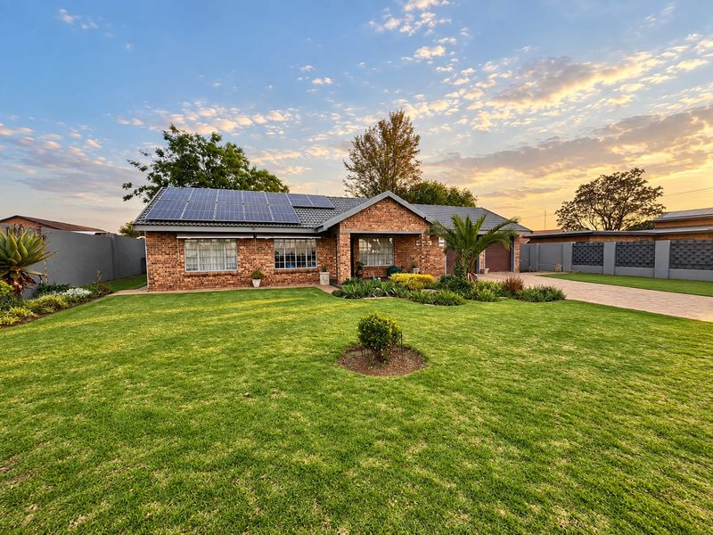 Well-maintained brick family home featuring a spacious front lawn, paved driveway, integrated garage, and roof-mounted solar panels under a clear sky.