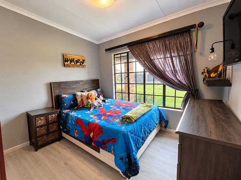 A well-maintained bedroom featuring light-toned laminate flooring, neutral wall finishes, and a large steel-framed window overlooking the garden.