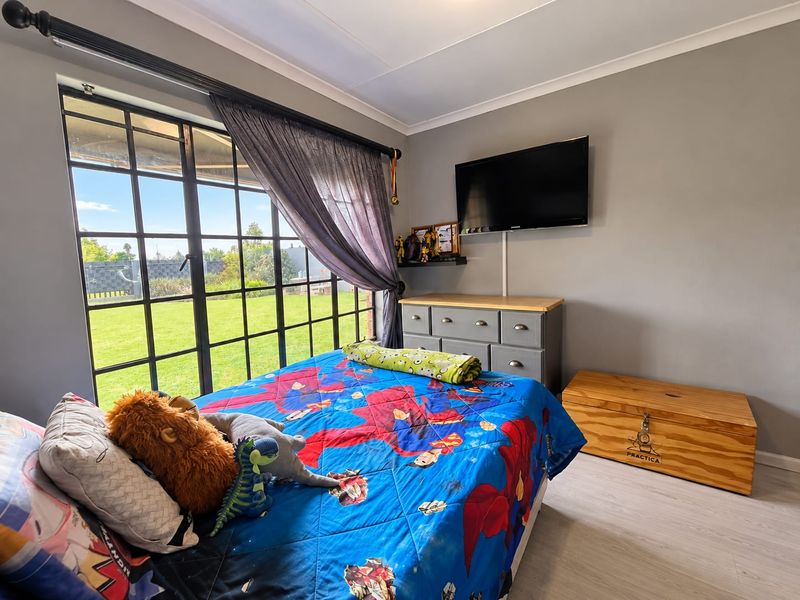 A well-maintained bedroom featuring large grid-style metal windows providing natural light and views of the garden, complemented by neutral grey walls and laminate flooring.