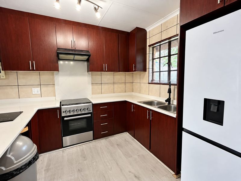 A well-maintained kitchen featuring dark wood cabinetry, white stone countertops, a stainless steel stove with extractor, and modern laminate flooring.