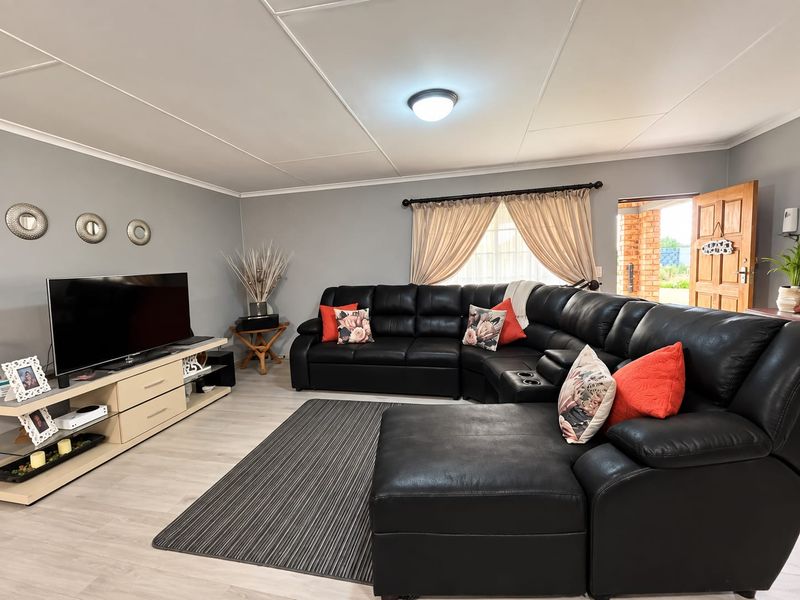 A well-maintained living room featuring light laminate flooring, a tiled ceiling, and a wooden exterior door leading to the garden.