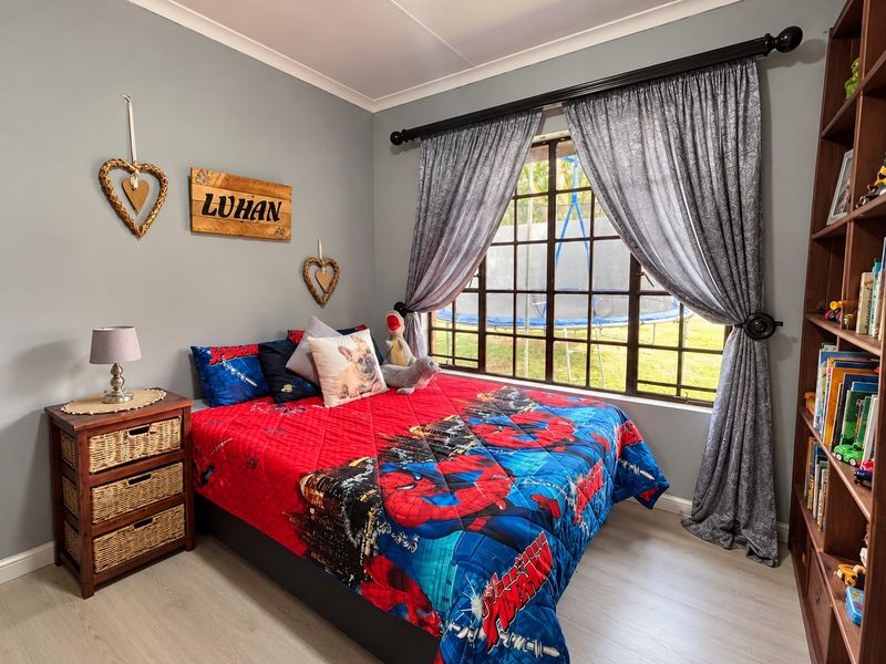 A well-maintained bedroom featuring laminate flooring, a grid-pattern window with curtains, and a built-in shelving unit.