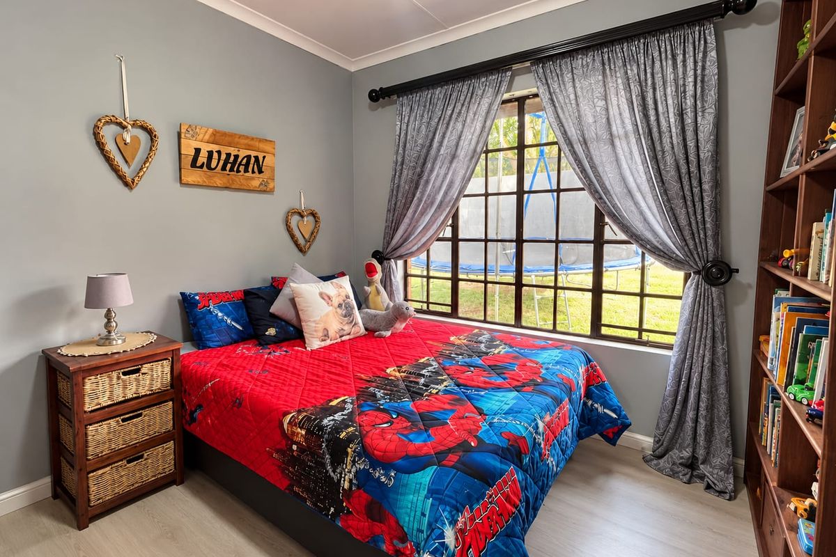 A well-maintained bedroom featuring laminate flooring, a grid-pattern window with curtains, and a built-in shelving unit.