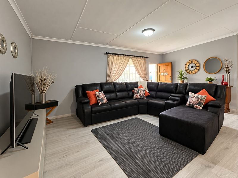 A well-maintained living room featuring light-toned laminate flooring, neutral grey walls, and a coved ceiling with a central light fixture.