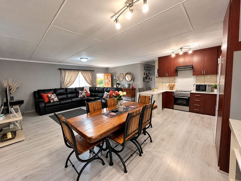 Spacious open-plan living area featuring a modern kitchen with dark wood cabinetry, a central island, and light-toned laminate flooring throughout the dining and lounge space.