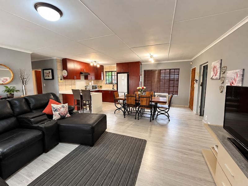 Spacious open-plan living and dining area featuring modern laminate flooring, a functional kitchen with built-in cabinetry, and a central island.