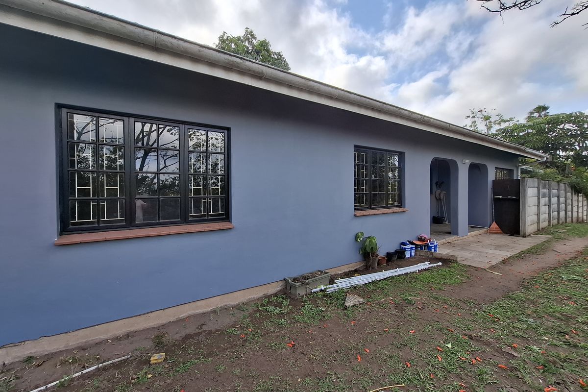 Rear exterior view of the house featuring blue painted walls, dark-framed windows with security bars, and a concrete patio area.