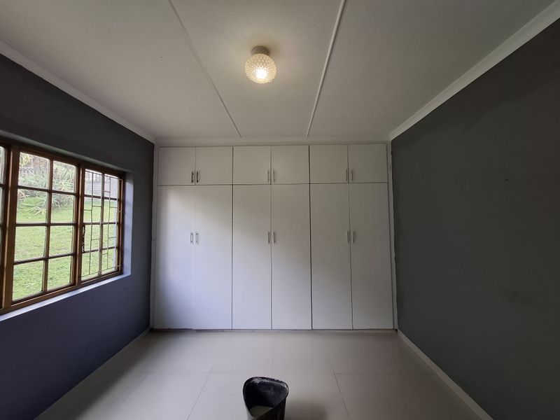A clean, empty bedroom featuring neutral tiled flooring, dark grey walls, and extensive white built-in cupboards for ample storage.