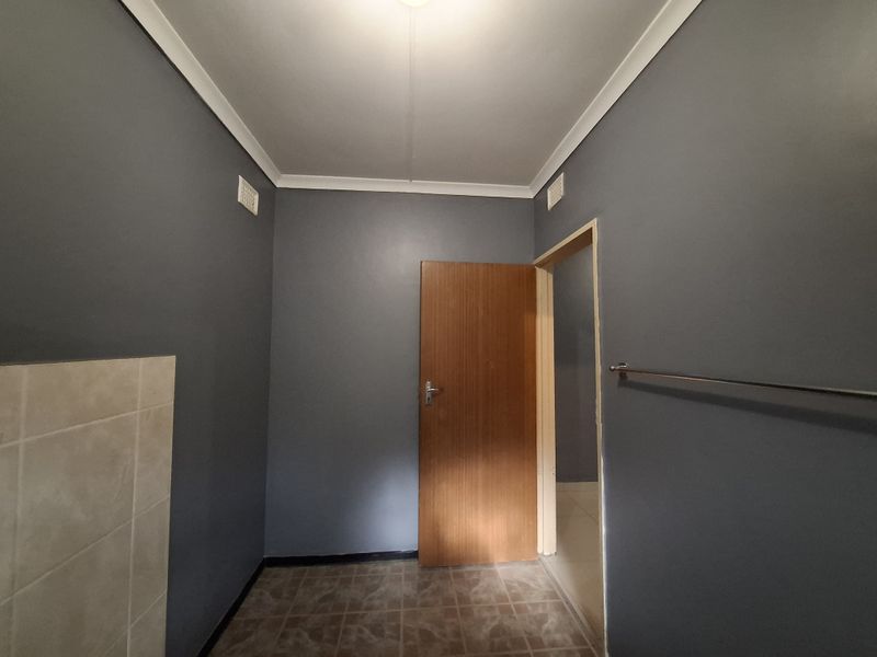 A clean, empty laundry room featuring dark grey walls, tiled flooring, and a tiled splashback area, providing a functional utility space.