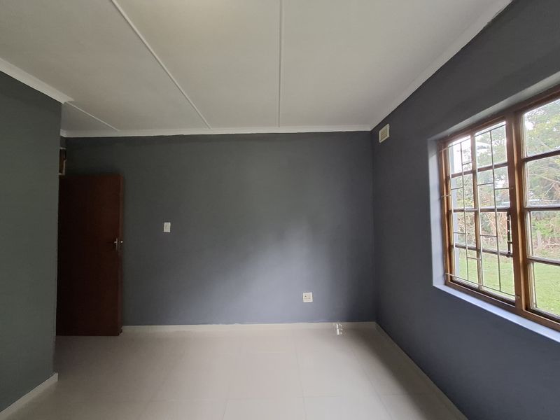 A clean, empty bedroom featuring neutral grey walls, tiled flooring, and a timber-framed window with security bars.