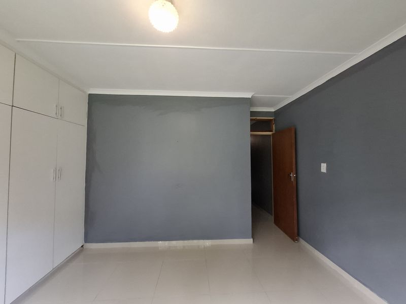 An empty bedroom featuring tiled flooring, built-in cupboards, and grey painted walls with a neutral ceiling finish.