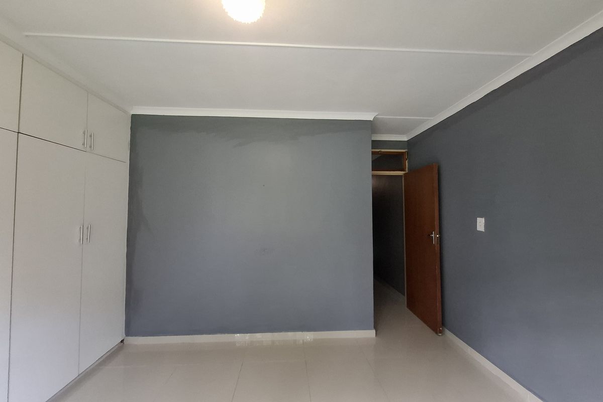 An empty bedroom featuring tiled flooring, built-in cupboards, and grey painted walls with a neutral ceiling finish.