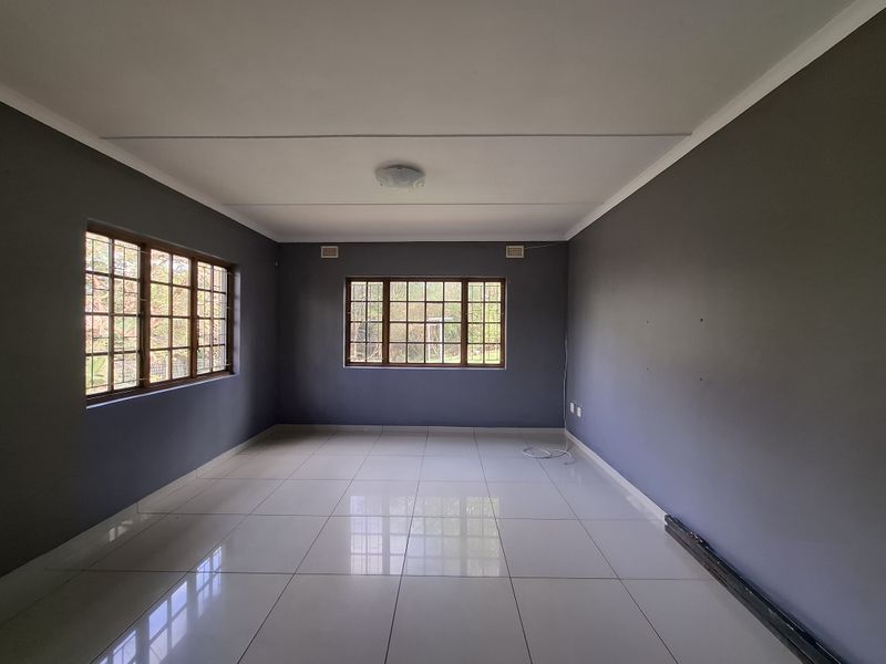 A spacious, empty living room featuring neutral grey walls, large timber-framed windows, and polished white floor tiles.