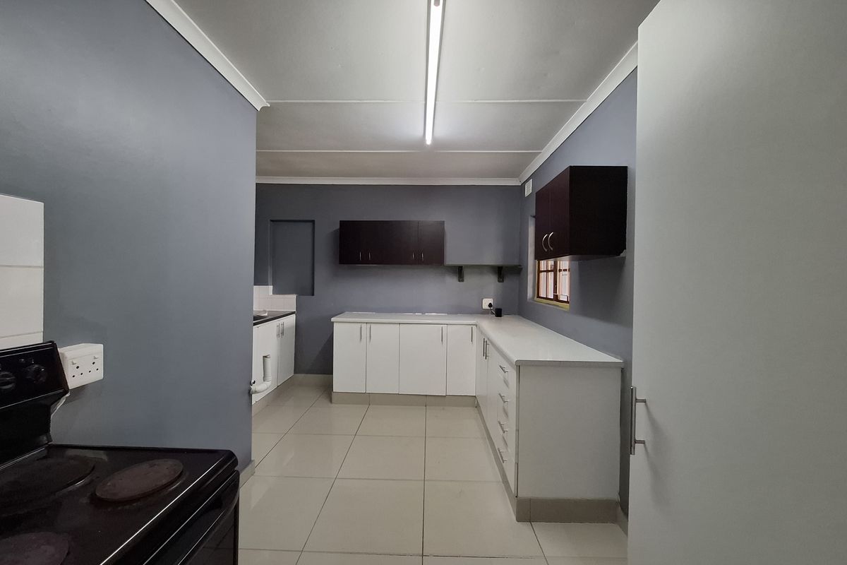 A functional kitchen featuring white base cabinetry, dark wall-mounted cupboards, tiled flooring, and an electric stove, offering a clean and practical workspace.
