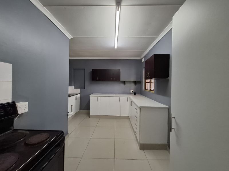 A functional kitchen featuring white base cabinetry, dark wall-mounted cupboards, tiled flooring, and an electric stove, offering a clean and practical workspace.