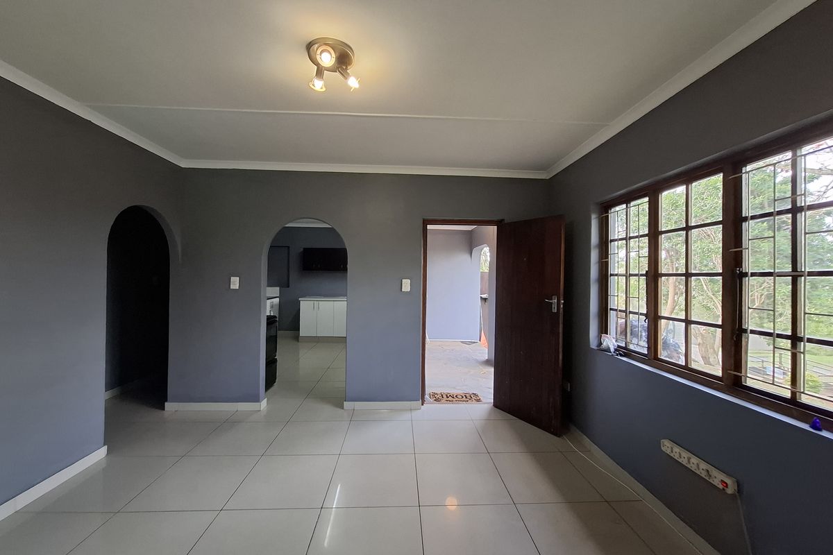 An empty living room featuring tiled flooring, arched doorways, and large windows with security bars, offering a neutral canvas for interior design.