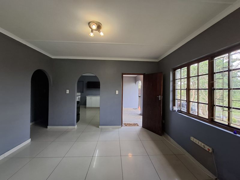 An empty living room featuring tiled flooring, arched doorways, and large windows with security bars, offering a neutral canvas for interior design.