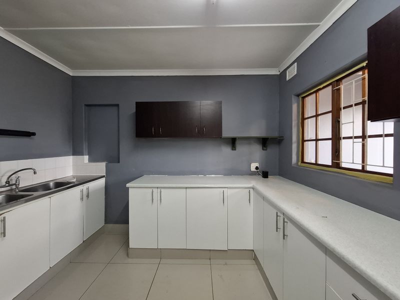A functional kitchen featuring white base cabinets, dark upper cupboards, laminate countertops, and a stainless steel sink, offering a clean canvas for updates.