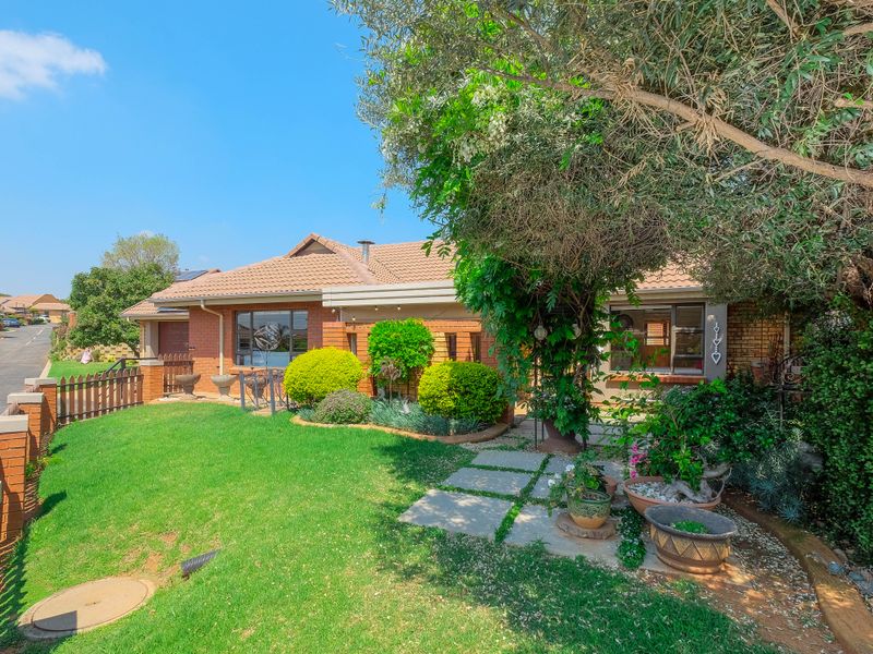 A well-maintained front exterior view of a brick retirement village home featuring a landscaped garden, paved walkway, and secure boundary fencing.
