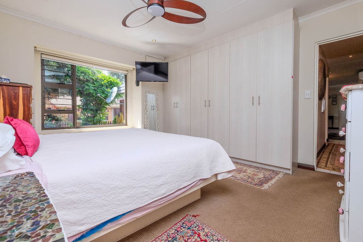 A well-maintained bedroom featuring extensive built-in wardrobes, a ceiling fan, and large windows providing natural light and garden views.