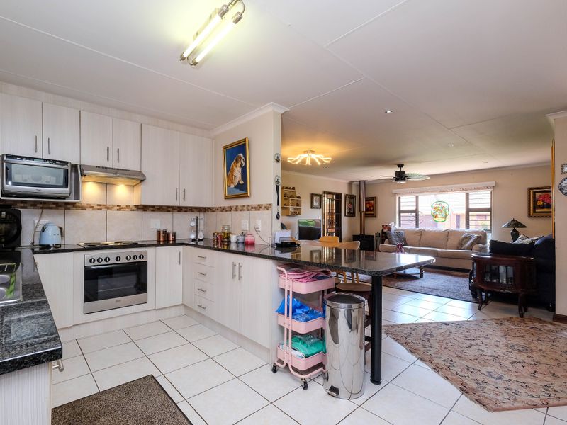 Open-plan kitchen and living area featuring light-toned cabinetry, granite countertops, integrated appliances, tiled flooring, and a cozy wood-burning stove in the lounge.