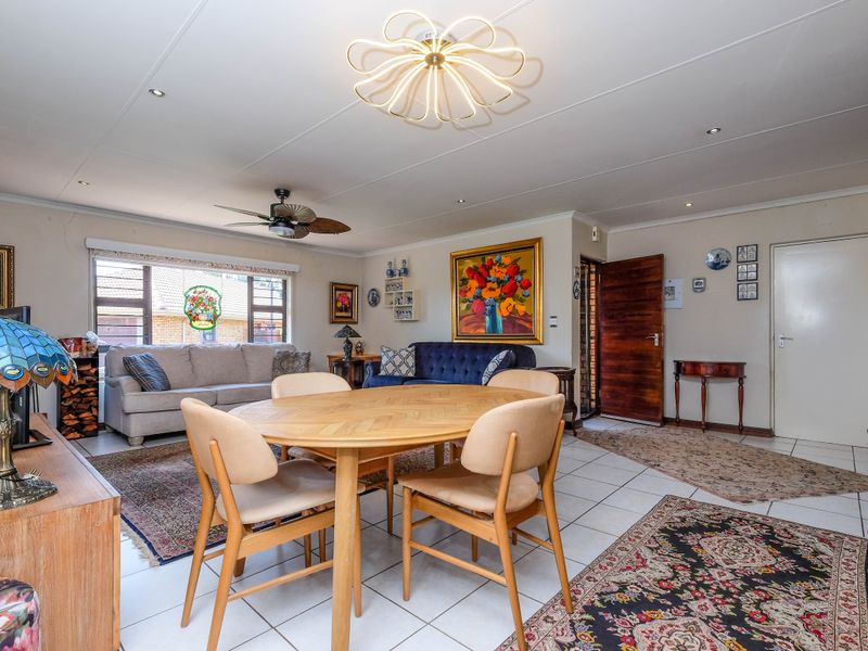 Spacious open-plan living and dining area featuring tiled flooring, a wood-burning fireplace, and modern ceiling lighting in a well-maintained retirement village unit.