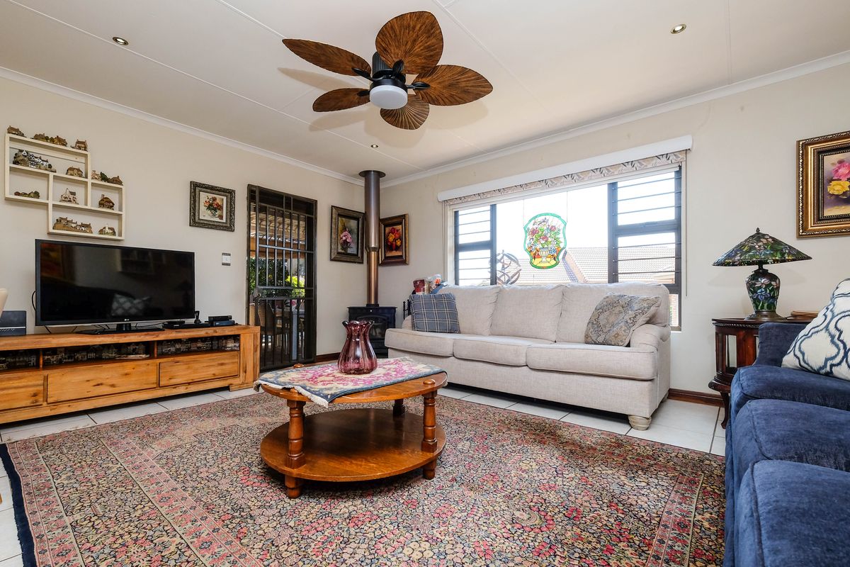 A comfortable living room featuring a wood-burning stove, ceiling fan, tiled flooring, and large windows providing natural light.