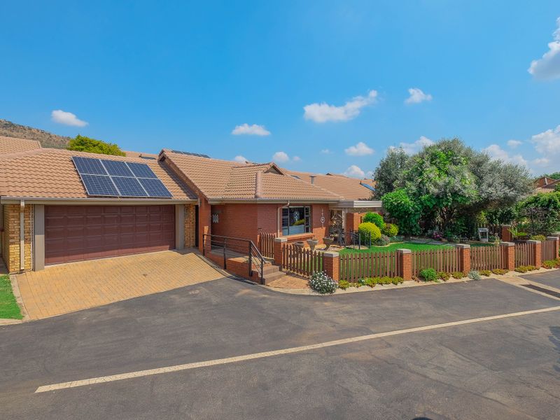A well-maintained retirement village residence featuring a brick facade, tiled roof, solar panels, paved driveway, and a private fenced garden area.