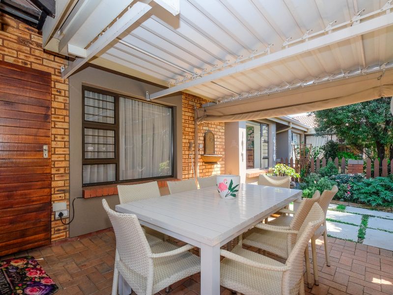 A covered outdoor patio area featuring brick paving, an exposed brick wall, and a retractable awning, providing a comfortable space for outdoor dining.