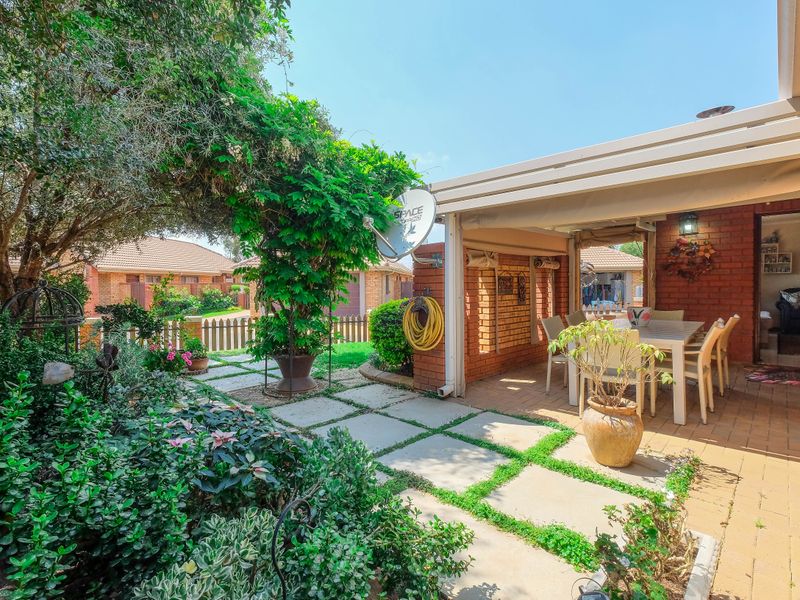 A well-maintained covered patio area featuring brick walls and paved flooring, seamlessly connecting to a lush, landscaped garden space.
