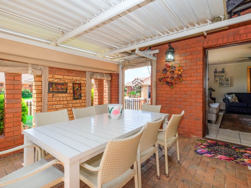 A covered outdoor patio featuring exposed brick walls, brick paver flooring, and a corrugated metal roof, providing a comfortable space for outdoor dining.