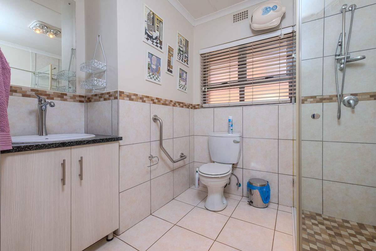 A functional bathroom featuring a vanity with granite countertop, a walk-in shower, and a wall-mounted grab rail for accessibility.