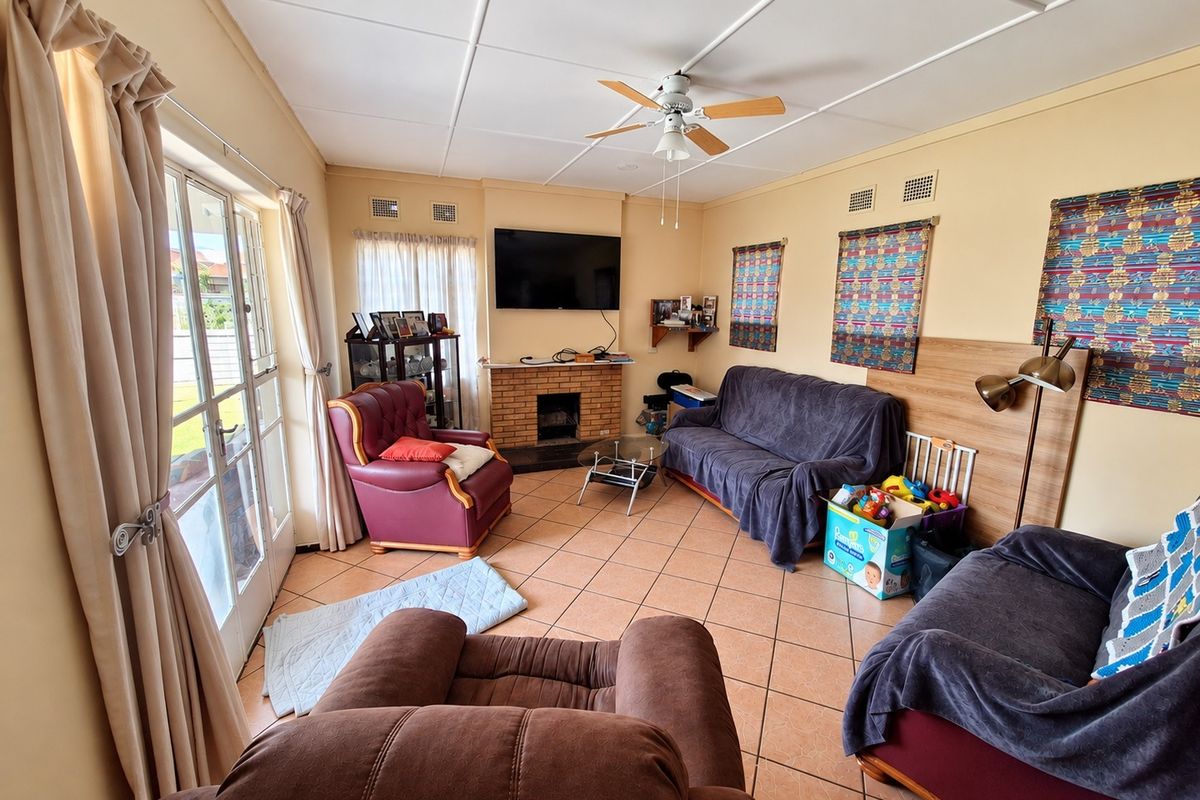 A living room featuring a brick fireplace, tiled flooring, and a ceiling fan, with direct access to the exterior through glass sliding doors.