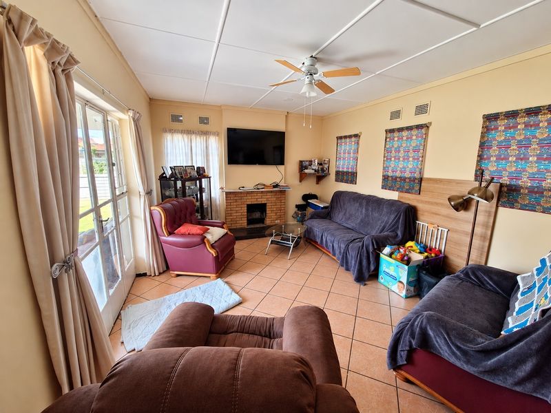 A living room featuring a brick fireplace, tiled flooring, and a ceiling fan, with direct access to the exterior through glass sliding doors.