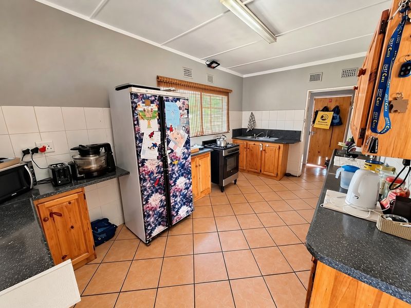 A functional kitchen featuring wooden cabinetry, laminate countertops, a double sink, and tiled flooring, offering a practical layout with potential for modern updates.