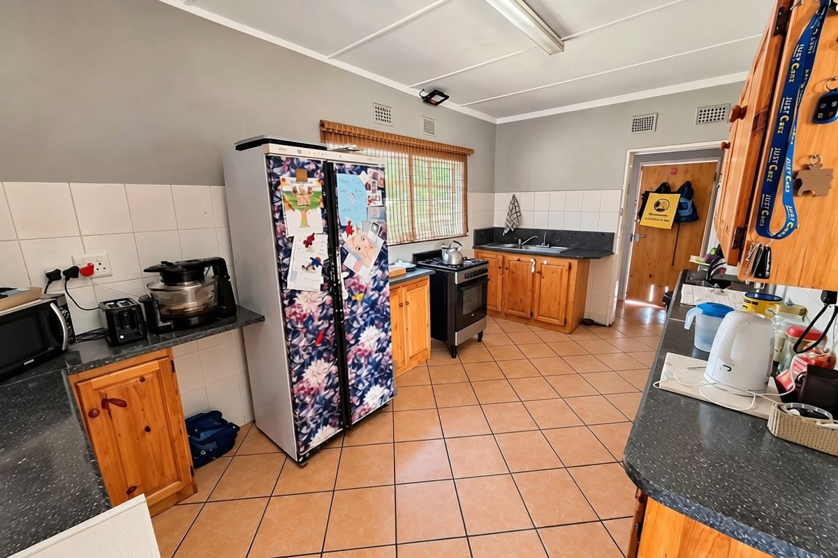A functional kitchen featuring wooden cabinetry, laminate countertops, a double sink, and tiled flooring, offering a practical layout with potential for modern updates.