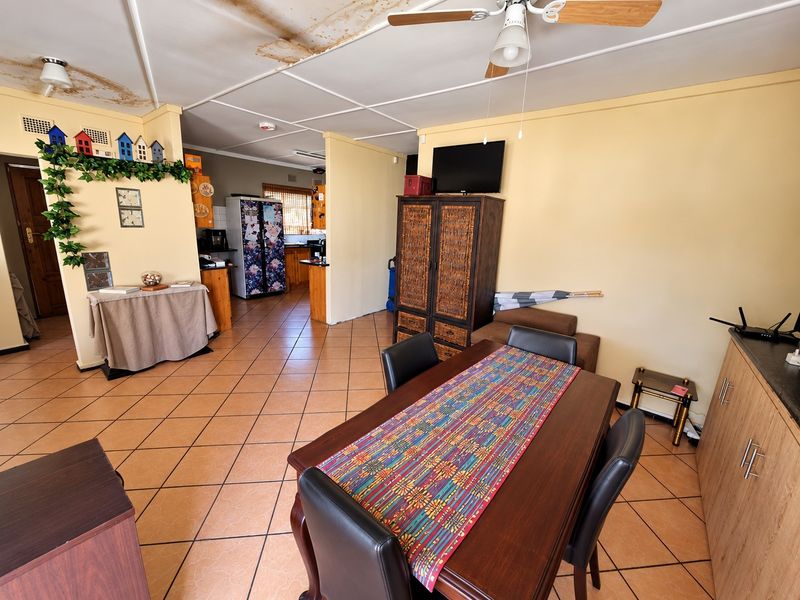 Open plan living and dining area featuring tiled flooring and ceiling fan, with visible water damage on the ceiling panels requiring maintenance.
