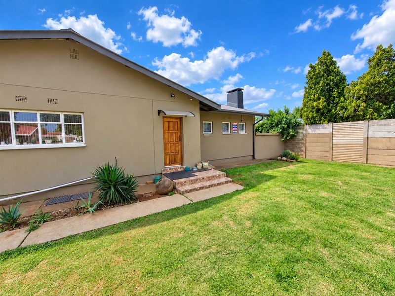 Rear view of the house featuring a lawn, concrete pathway, tiled entrance steps, and a prominent external chimney against a boundary wall.