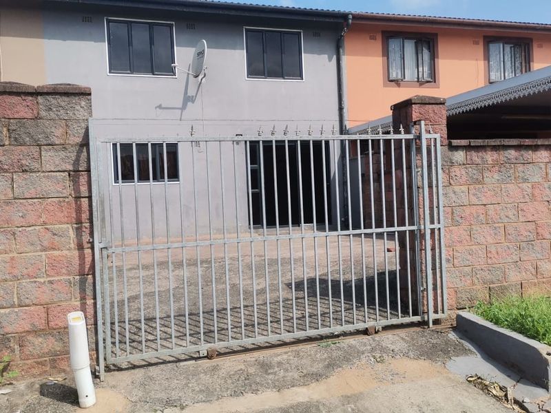 Front view of a residential property featuring a brick boundary wall, metal sliding gate, and paved driveway area.