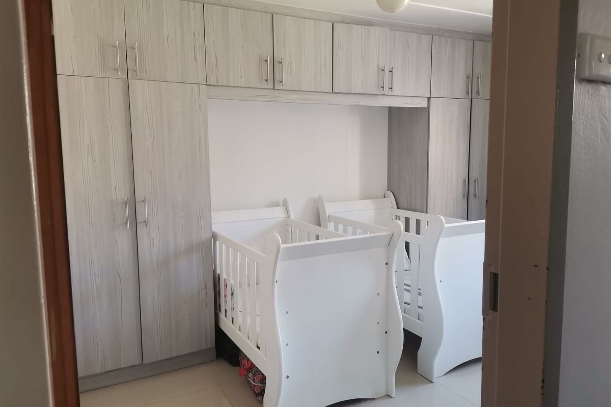A bedroom featuring extensive built-in cabinetry with light wood-grain finish and neutral tiled flooring.