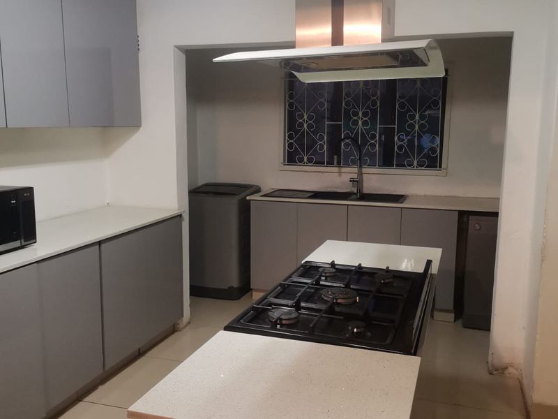 Modern kitchen featuring grey cabinetry, stone countertops, a central island with a gas hob, and a stainless steel extractor fan.