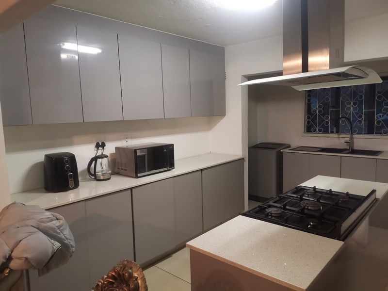 Modern kitchen featuring sleek grey cabinetry, stone countertops, a central island with a gas hob, and a stainless steel extractor fan.