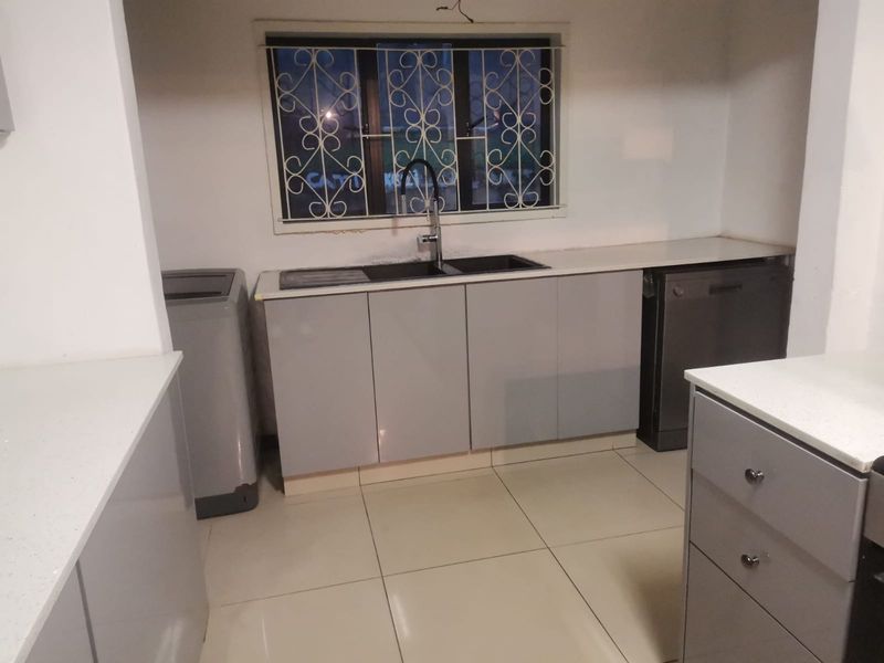 Modern kitchen featuring grey cabinetry, white quartz countertops, double basin sink, and tiled flooring, with security bars on the window.