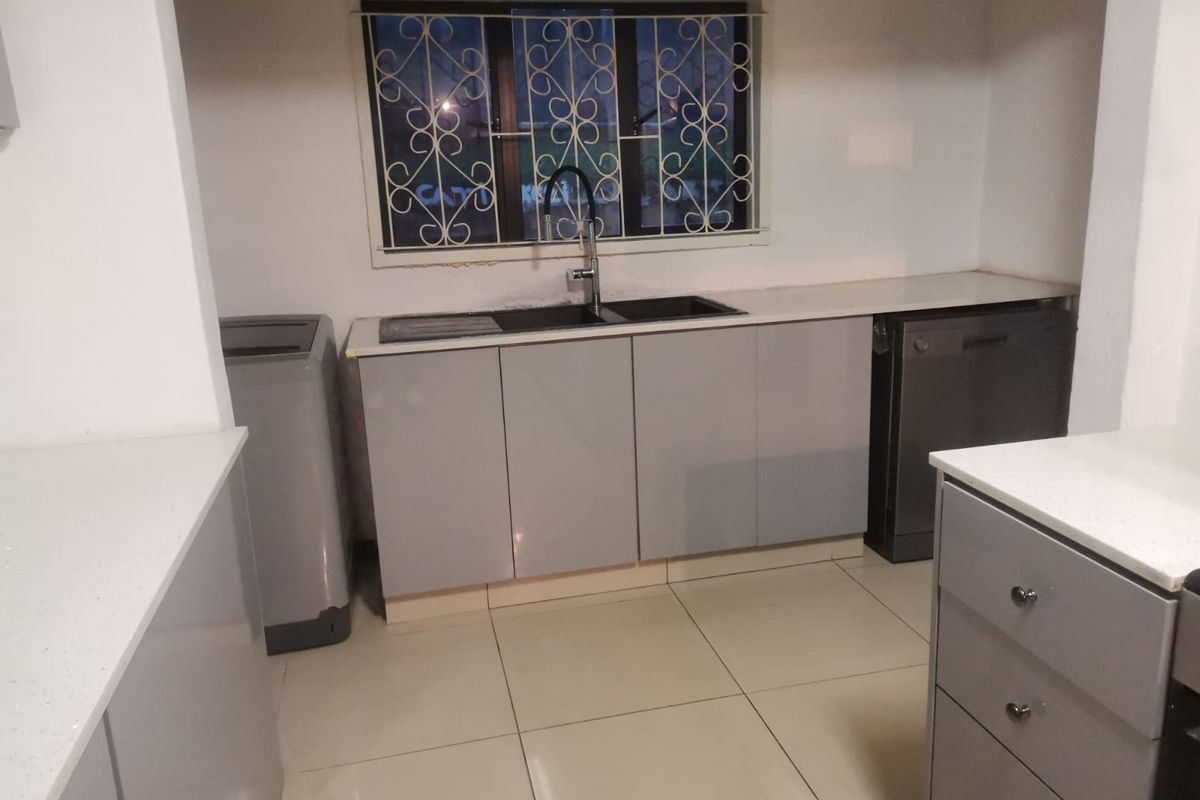 Modern kitchen featuring grey cabinetry, white quartz countertops, double basin sink, and tiled flooring, with security bars on the window.