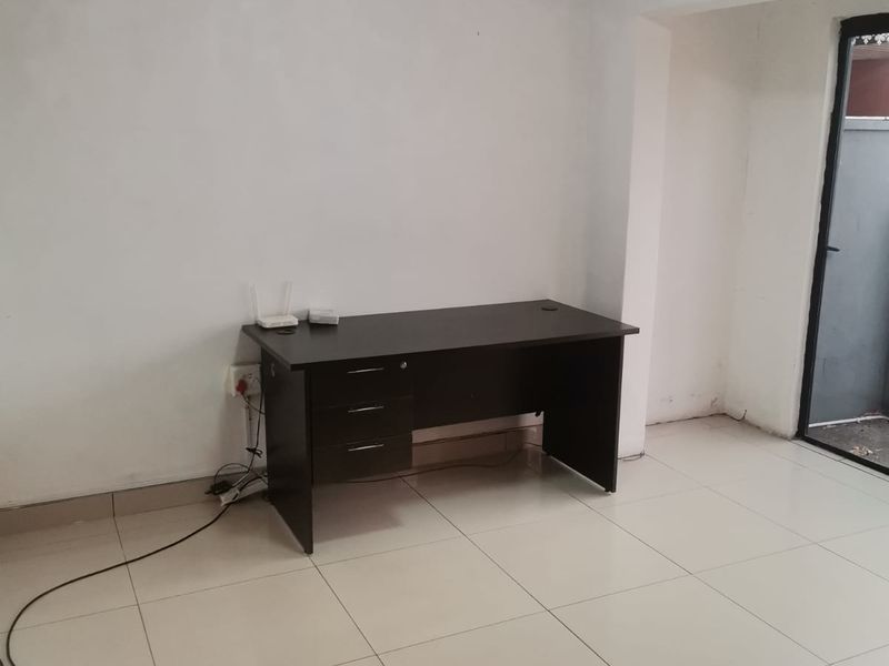 A bright, empty office space featuring neutral tiled flooring and direct access to an outdoor area through a glass door.